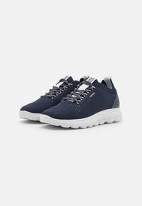 Marina andningsbara stickade sneakers med vit gummisula, texturerad ovandel och flerfärgade skosnören. Har en dragflik vid hälen.