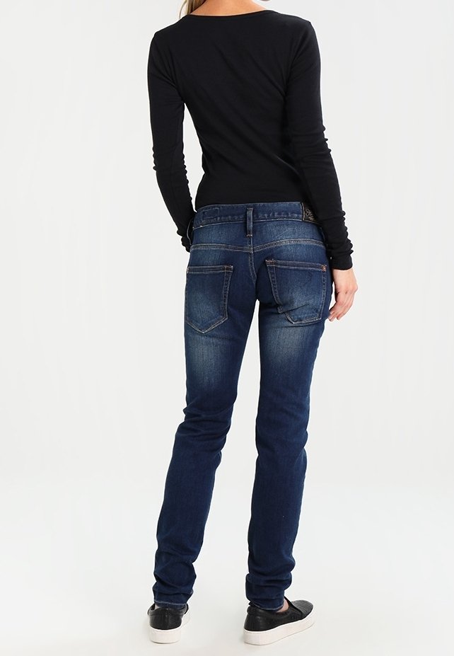 Jeans skinny blu scuro con una texture sbiadita e tasche posteriori tradizionali, abbinati a un top nero a maniche lunghe.