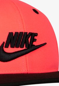 Sarkans beisbola cepure ar melnu izšūtu "NIKE" logo un svītru. Iespējo strukturētu kroni un plakanu maluru. Gluda auduma tekstūra.