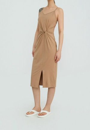 Beige midi-Kleid in figurbetonter Passform mit gedrehtem Vorderteil, verstellbaren dünnen Trägern und Frontschlitz, kombiniert mit weißen Flip-Flop-Sandalen.