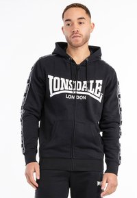Sudadera con cremallera negra en mezcla de algodón que presenta un gran logo blanco "LONSDALE LONDON" en la parte frontal y cinta blanca en contraste a lo largo de las mangas.