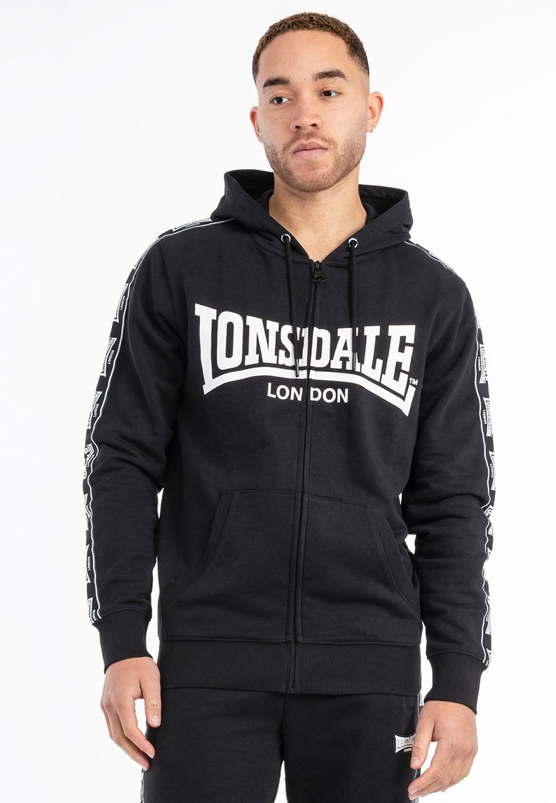 Sudadera con cremallera negra en mezcla de algodón que presenta un gran logo blanco "LONSDALE LONDON" en la parte frontal y cinta blanca en contraste a lo largo de las mangas.
