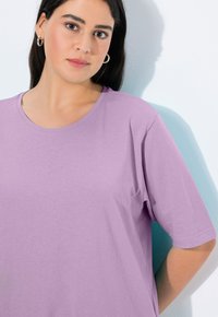 Lavendel-baumwoll T-Shirt mit glatter Textur, kurzen Ärmeln und rundem Halsausschnitt. Flach auf einen hellen Hintergrund gelegt.