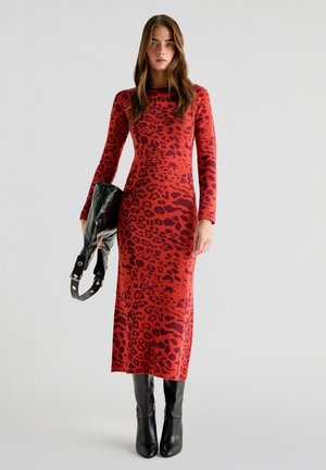 Robe ajustée à imprimé léopard rouge avec des manches longues, arrivant au genou. Bottes noires montantes et un sac à main noir avec des accents en métal argenté.