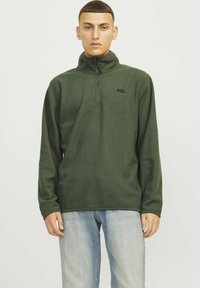 Pullover in pile verde oliva con colletto alto, zip a un quarto e dettaglio logo nero sul petto. Maniche lunghe e texture morbida.