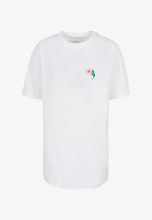 Biała bawełniana koszulka z krótkim rękawem, z okrągłym dekoltem oraz różowym wzorem kwiatu z zielonymi liśćmi po lewej stronie klatki piersiowej.