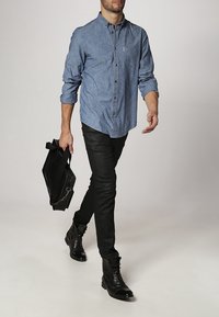 Camisa vaquera abotonada en azul claro, mangas largas remangadas, combinada con vaqueros negros y botas negras con cordones. Lleva un bolso negro.