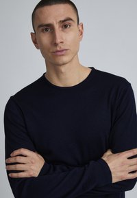 Tricou cu mânecă lungă, de culoare albastru închis, cu guler rotund, fabricat dintr-un material texturat, având un design ajustat și detalii fine cu margeană la manșete.