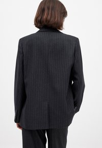 Blazer noir à rayures, au design structuré, avec une fente unique, des revers crantés et des poignets boutonnés. Texture de tissu lisse.