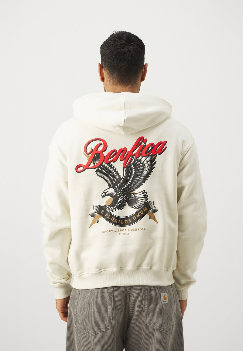 Hoodie crème mettant en avant un grand graphisme d'aigle, "Benfica" en écriture rouge, et une bannière avec "E Pluribus Unum" dans le dos.