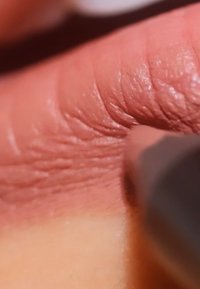 Cosmetic pencil applying creamy, nude pink color on textured skin, highlighting fine lines and natural tones of the palm.