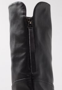 Bota alta hasta la rodilla de cuero negro con acabado texturizado, que cuenta con una cremallera de longitud completa y una lengüeta de tirador decorativa en la parte superior.