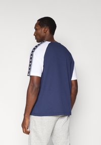 Μπλε ναυτικό t-shirt με λευκά μανίκια, διακοσμημένο με αντίθετη ραφή και ταινία λογότυπου κατά μήκος των ώμων. Μαλακό βαμβακερό υλικό, κανονική εφαρμογή.