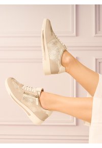 Baskets beiges en tissu métallique texturé, semelle blanche, devant lacé et détail de zip sur le côté. Accents en cuir lisse au talon et à la pointe.