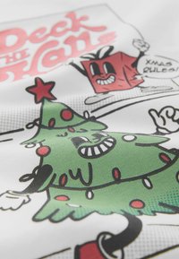 Balts audums ar karikatūras dizainu — zaļa Ziemassvētku eglīte ar sarkaniem rotājumiem un smaidīga sarkana dāvanu kaste, teksts "Deck the Halls".