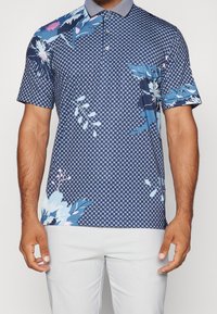 Polo de manga corta con base azul marino y patrones florales y geométricos contrastantes en azul y rosa, con un cuello texturizado.