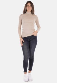 Maglione col dolcevita beige in materiale a costine, abbinato a jeans skinny scuri e sneaker bianche. Un outfit casual con design aderente e texture liscia.