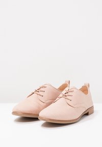 Chaussures oxford à lacets rose clair en cuir texturé, dotées d'un petit talon en bois et d'un design à bout arrondi.