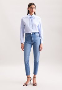 Camicia a righe azzurro chiaro con dettaglio a papillon, abbinata a jeans in denim chiaro a vita alta e sandali neri con tacco alto e fasce.