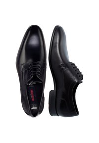 Schwarze Lederschuhe mit glatter Oberfläche, spitzer Vorderkappe, Schnürung vorne und kontrastierenden Nähten an den Seitenakzenten.