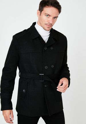 Black wool blend double-breasted coat with a belt, featuring shoulder epaulets, snap buttons, and two side pockets. High collar with white turtleneck.