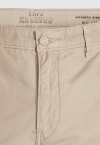 Pantalon beige Levi’s XX Chino avec fermeture à boutons et passants pour ceinture, taille W32 L32, avec des détails cousus sur la ceinture et la braguette.