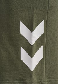 Tela verde oliva con una superficie texturizada presenta dos grandes formas de flecha blanca, dispuestas verticalmente, en el lado.