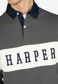 Maglietta da rugby grigia con colletto blu navy e fascia bianca con ricamo "HARPER" in blu scuro. Tessuto testurizzato con chiusura a due bottoni.