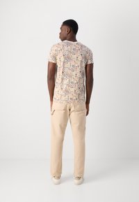 Kortærmet beige skjorte med et farverigt geometrisk mønster, parret med lyse beige bukser og beige sneakers med logoaccents.