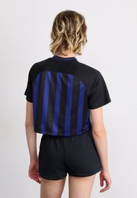 Black cropped athletic shirt with vertical blue stripes on the back, soft fabric, short sleeves, paired with black shorts.