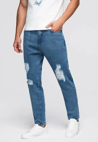 Vaqueros de mezclilla azul con detalles desgastados, diseño de pierna recta y un acabado ligeramente descolorido, combinados con zapatillas blancas.