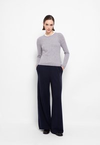 Maglione di lana grigio con scollo rotondo, abbinato a pantaloni larghi blu navy con tasche laterali. Texture lisce, design minimalista.