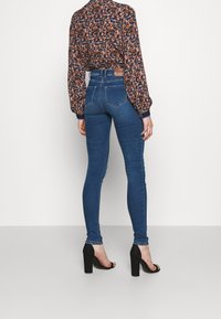 Hochtaillierte blaue Jeans mit einer figurbetonten Silhouette, aus Denim, mit Gesäßtaschen, kombiniert mit einer blumengemusterten Bluse und schwarzen Absätzen.