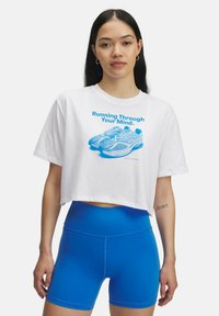 White cropped t-shirt with blue graphic print of shoes and text. Blue high-waisted shorts. Circular earrings visible.