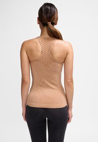 Béžové tílko s racerbackem s texturovaným vzorem na zádech a hladkým povrchem, doplněné tmavě šedými přiléhavými legínami.
