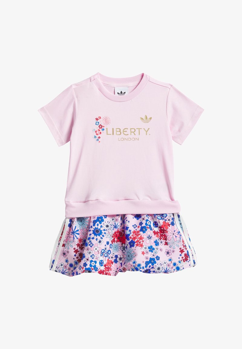 Różowy top z krótkim rękawem z złotym napisem „Liberty London” i kwiatowym haftem, zestawiony z różową spódnicą w kwiaty z niebieskimi i czerwonymi kwiatami.