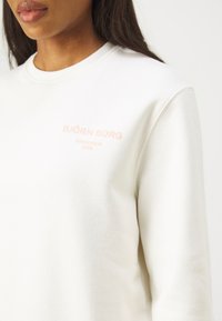 Felpa bianca con una consistenza morbida, caratterizzata da un testo ricamato di colore rosa che recita "BJÖRN BORG STOCKHOLM 1956" sul petto.