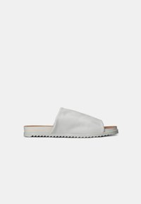 Bijele sandale na slip-on s glatkom kožnom gornjom stranom, teksturiranim potplatom i širokim trakama. Minimalistički estetski izgled s ravnim profilom.