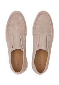 Zamszowe buty typu slip-on w jasnobeżowym kolorze, z nieco podwyższoną białą podeszwą, akcentami w postaci przeszyć oraz gładką podszewką wewnętrzną.