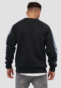Sudadera negra con mangas raglán, que presenta acentos laterales en azul claro y puños de canalé. La tela parece suave y ligeramente texturizada.