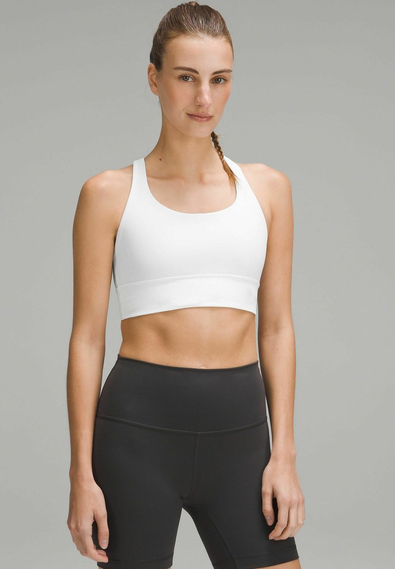 White athletic crop top with a wide neckline and racerback design paired with high-waisted black shorts; smooth, stretchy fabric.