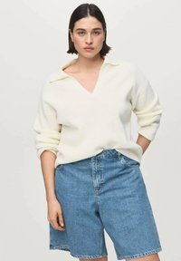 Pulover crem din tricot cu dungi, cu decolteu în V și guler pliat, asortat cu pantaloni scurți din denim albastru deschis, cu croială lejeră și cusături vizibile.