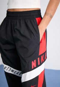 Black and red Nike sport pants featuring an elastic waistband, side pockets, and bold "NIKE" logo with white stripe detailing.