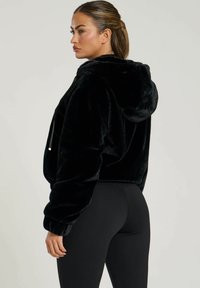 Czarna, skrócona bluza z kapturem z miękkiego materiału, z kieszeniami z przodu i sznurkami do regulacji. W zestawie z czarnymi legginsami.