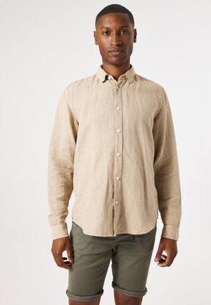 Lichtbeige linnen overhemd met lange mouwen, voorzien van een gebogen zoom en witte knopen, gecombineerd met opgerolde olijfgroene shorts.