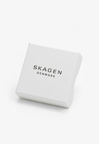 Bílá obdélníková krabice s zaoblenými hranami, na jejíž přední straně je černý nápis "SKAGEN DENMARK". Hladký povrch.