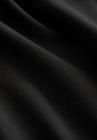 Musta teksturoidun kankaan pinta, joka on sileä ja kudottu, näyttäen hienovaraisia taitteita ja laskoksia, korostaen syvyyttä ja materiaalin laatua.