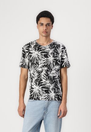 T-shirt noir avec imprimé de feuilles de palmier blanches, encolure ronde, manches courtes et coupe décontractée. Porté avec un jean en denim bleu clair.
