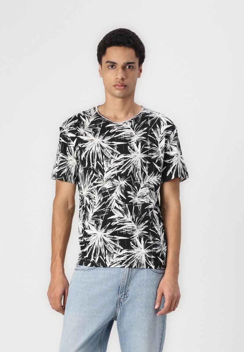 Sort t-shirt med hvid palmebladprint, rund halsudskæring, korte ærmer og afslappet pasform. Bæres med lysblå denimjeans.