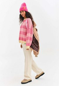 Pletený sveter s ružovými a béžovými pruhmi, žltý lem; hnedá prešívaná bunda; krémové široké nohavice; ružová čiapka; hnedé turistické topánky.